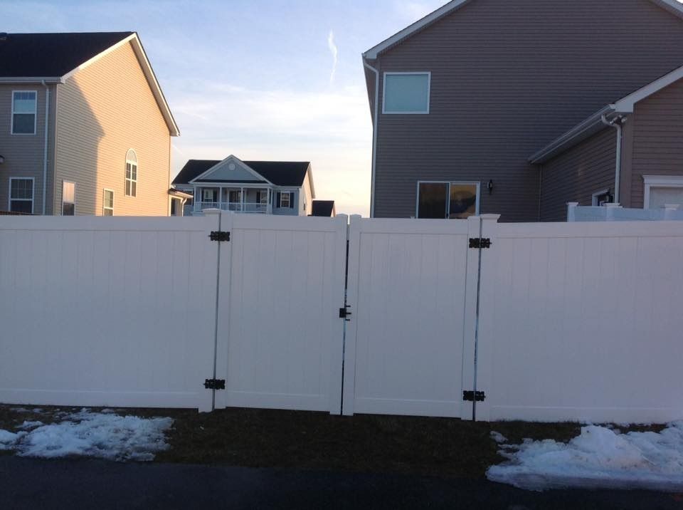 White fenced yard between houses with a gate and patches of snow on the ground