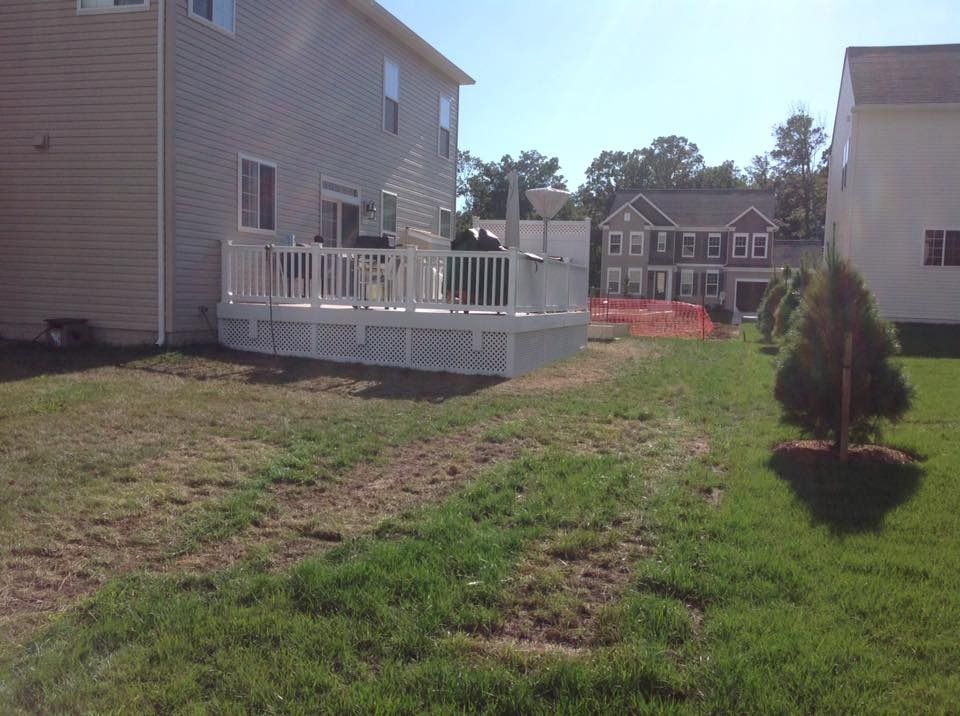 Backyard with a white deck beside a beige house, grassy yard, and apartment buildings in the distance