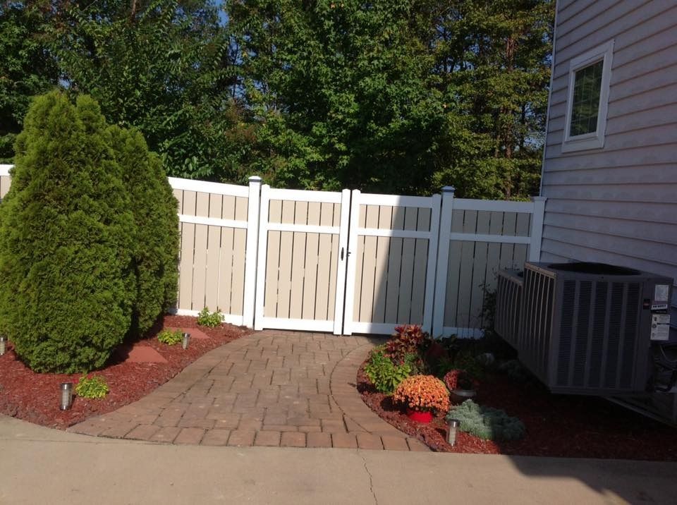 Backyard patio with white fence, paved walkway, shrubs, flowers, and an air conditioner unit.