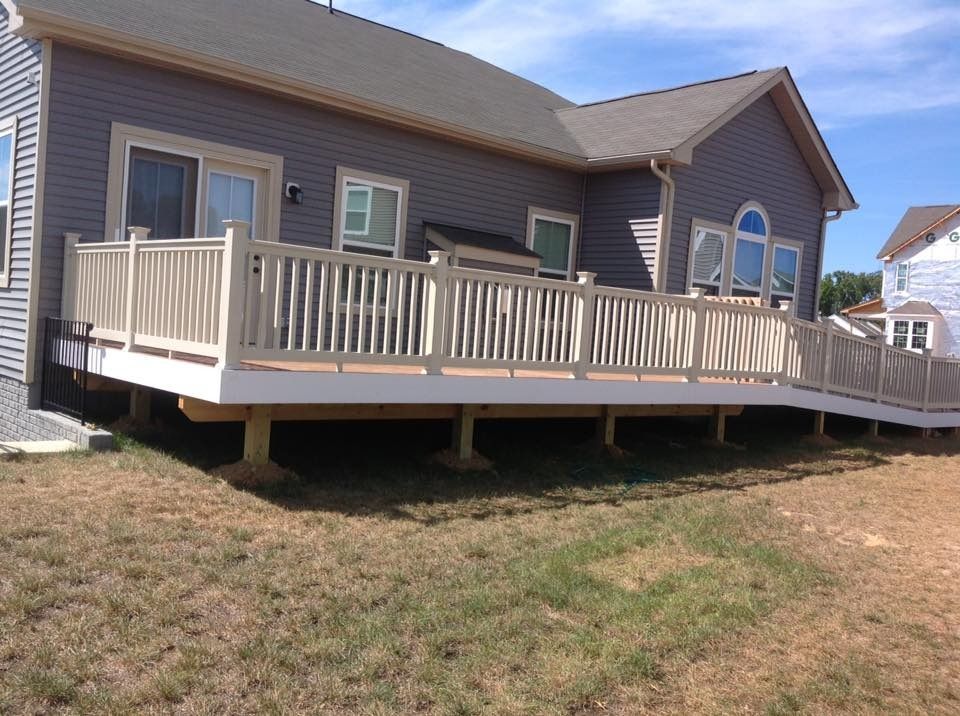 Side view of a tan house with a raised wooden deck and railing on a grassy yard