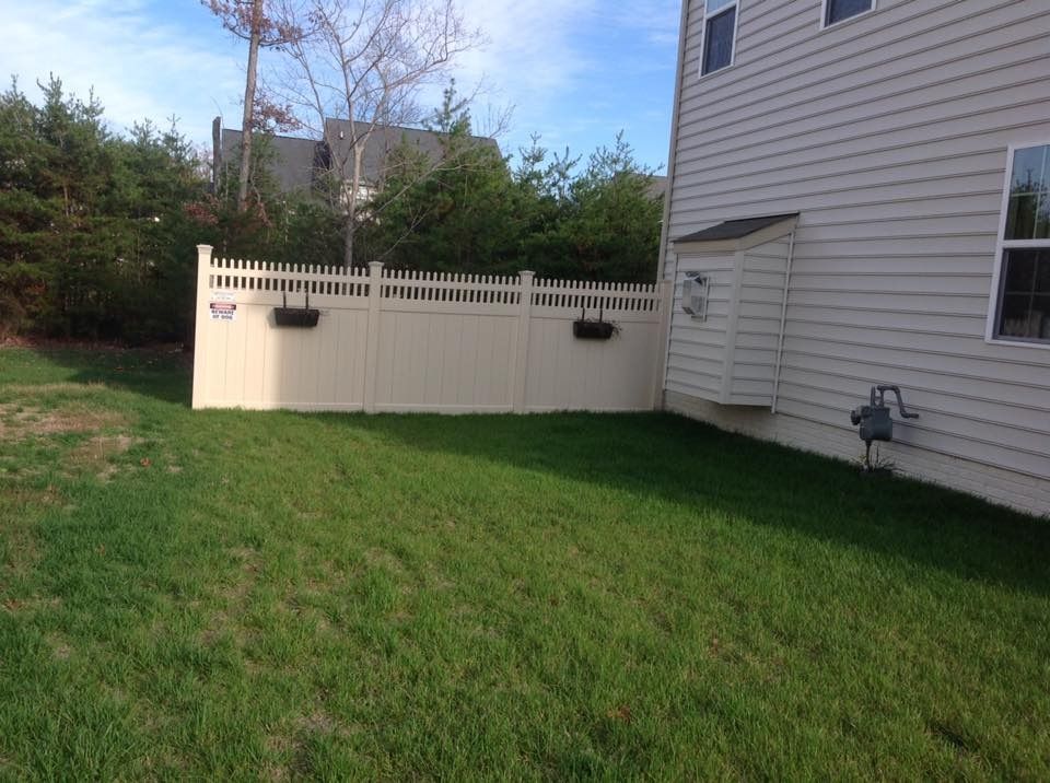 Backyard with green lawn, white fence, and side of a beige house under a blue sky
