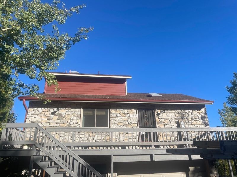 Stone house with red roof and wooden deck under a bright blue sky