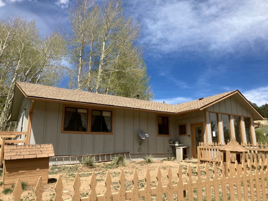 Single-story tan house with a fenced yard under a blue sky and trees