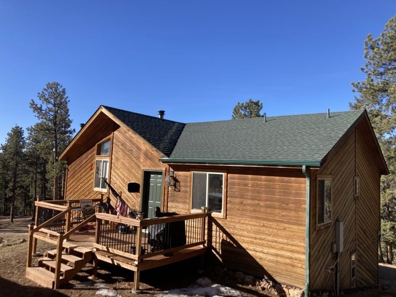Wooden cabin with a deck and railings in a pine forest under a clear blue sky