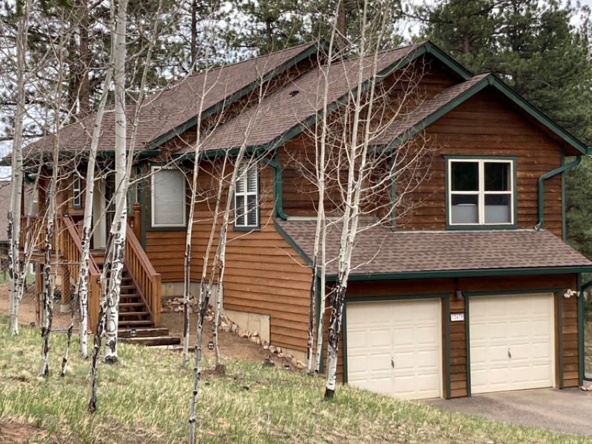 Wooden house with brown siding, dormer windows, and a two-car garage among birch trees