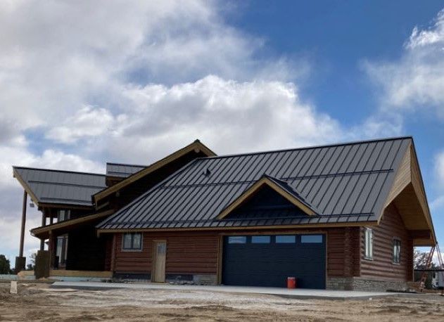 Brown wooden lodge with dark metal roof and garage under a cloudy sky
