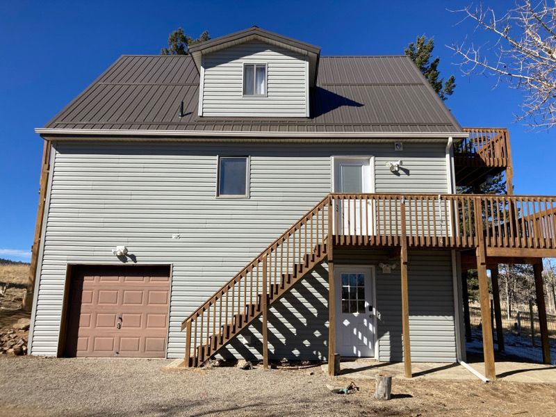 Two-story gray house with brown garage and outdoor wooden stairway, viewed from the back yard