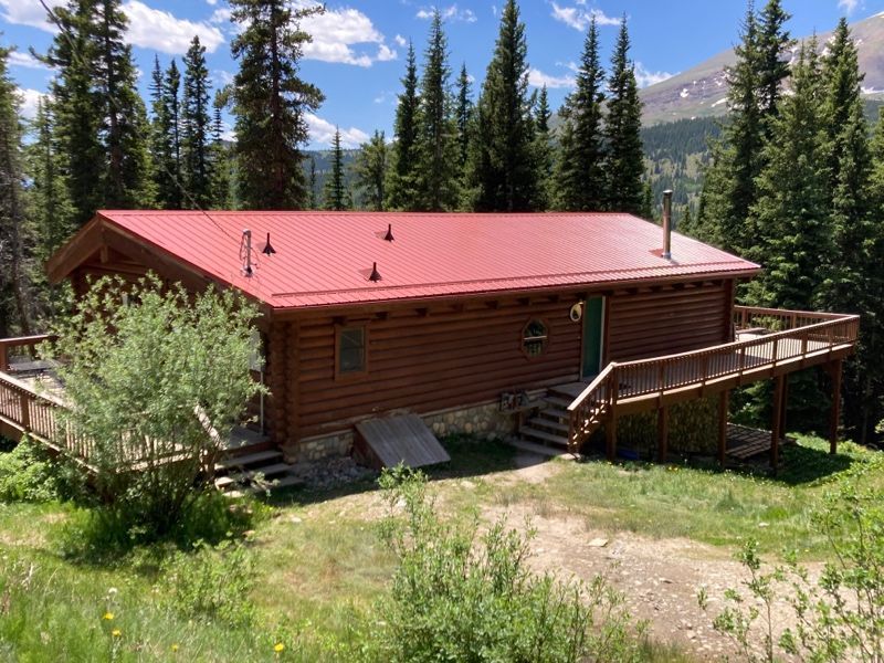 Rustic log cabin with a red roof and deck in a forested mountain setting