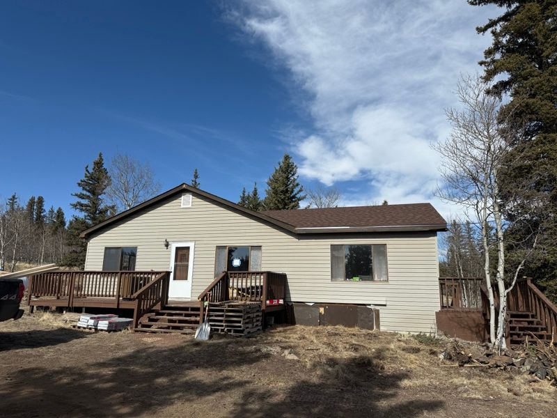 Single-story beige house with a wooden deck, set among trees under a blue sky.