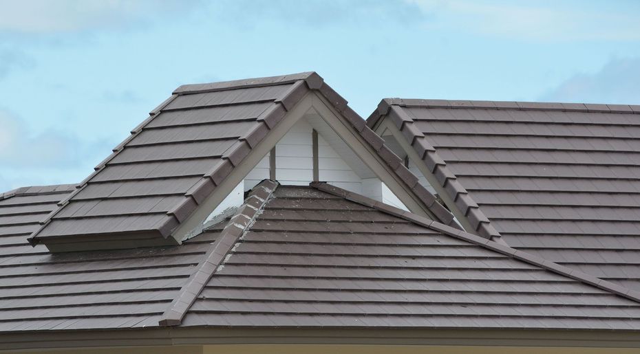 Close-up of a gray tiled roof with a dormer and blue sky in the background
