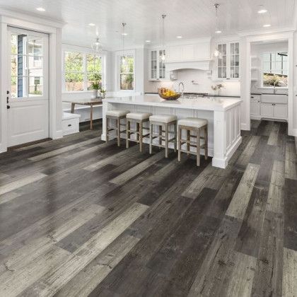 A kitchen with a large island and stools and a wooden floor.