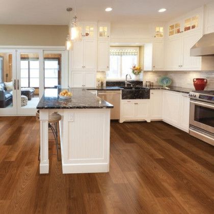 A kitchen with hardwood floors , white cabinets , stainless steel appliances and a large island.