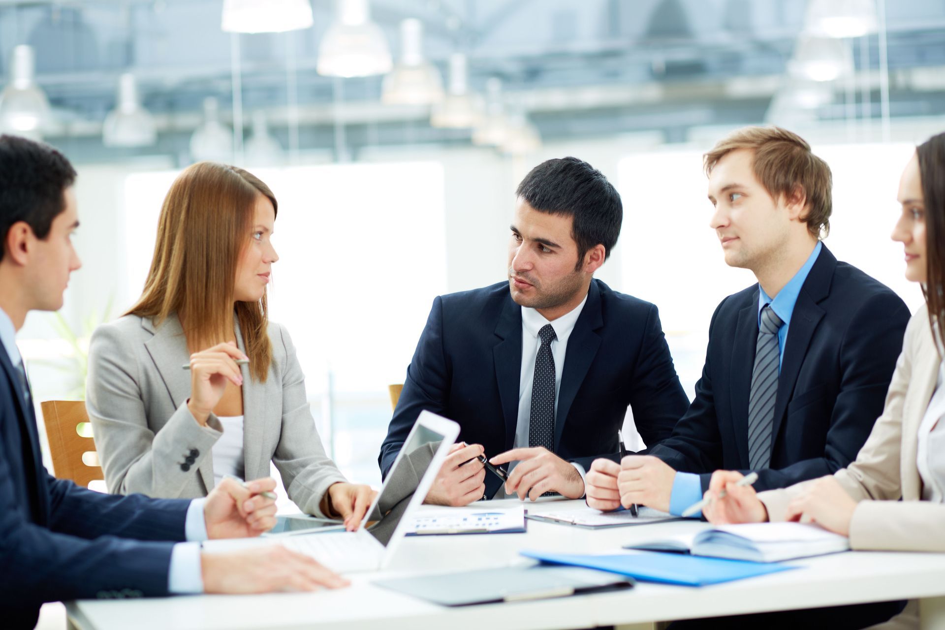 Business team in suits at a table, discussing and looking at documents in a bright office.