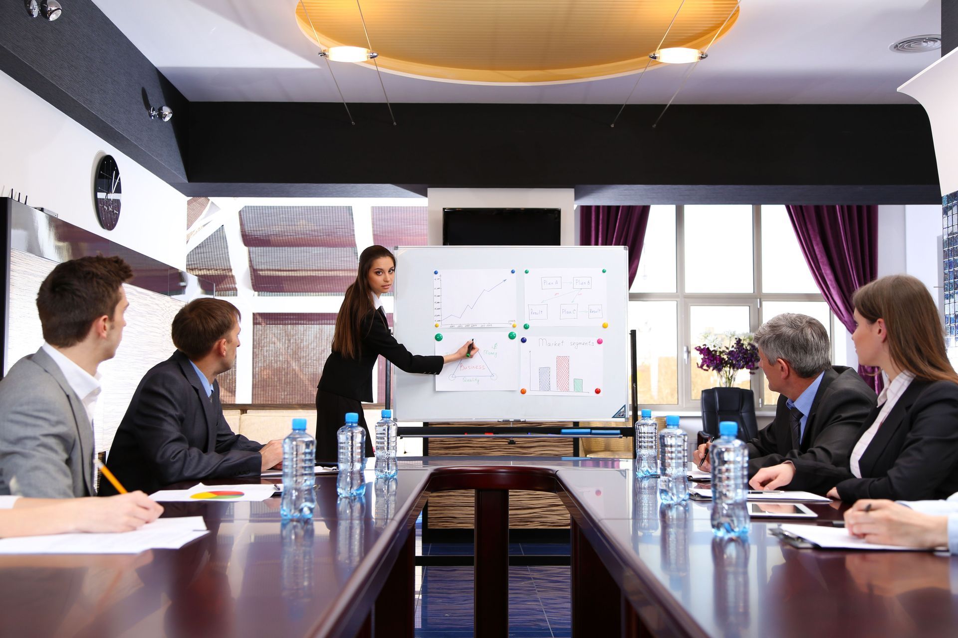 Businesswoman presenting at a whiteboard to a group in a conference room.