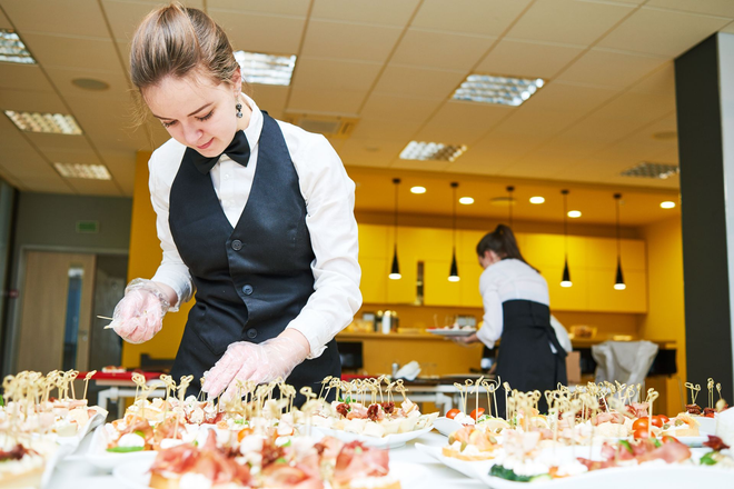 Woman in uniform arranging appetizers on a table at a catering event.
