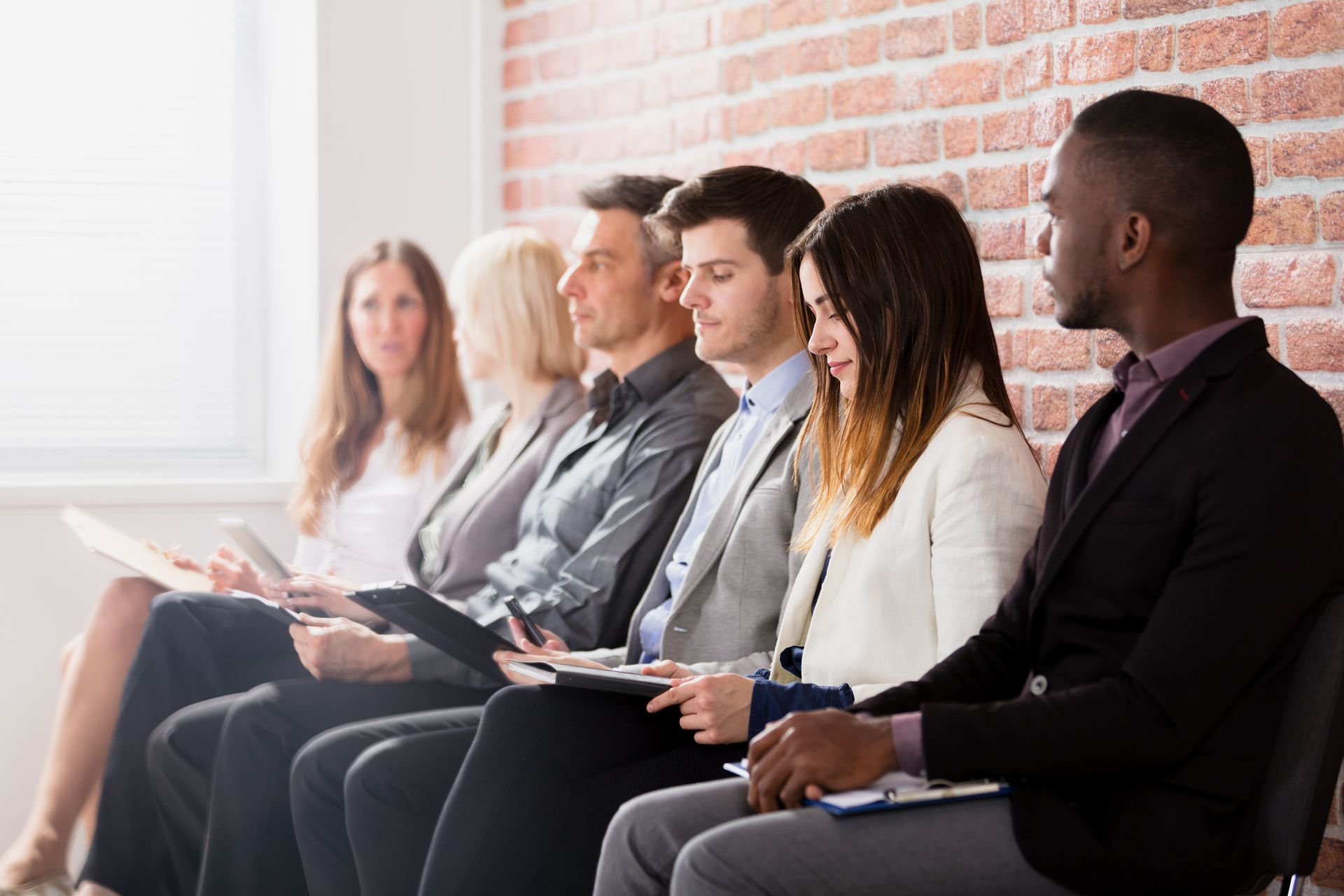People seated in a row, looking at papers. Brick wall background.