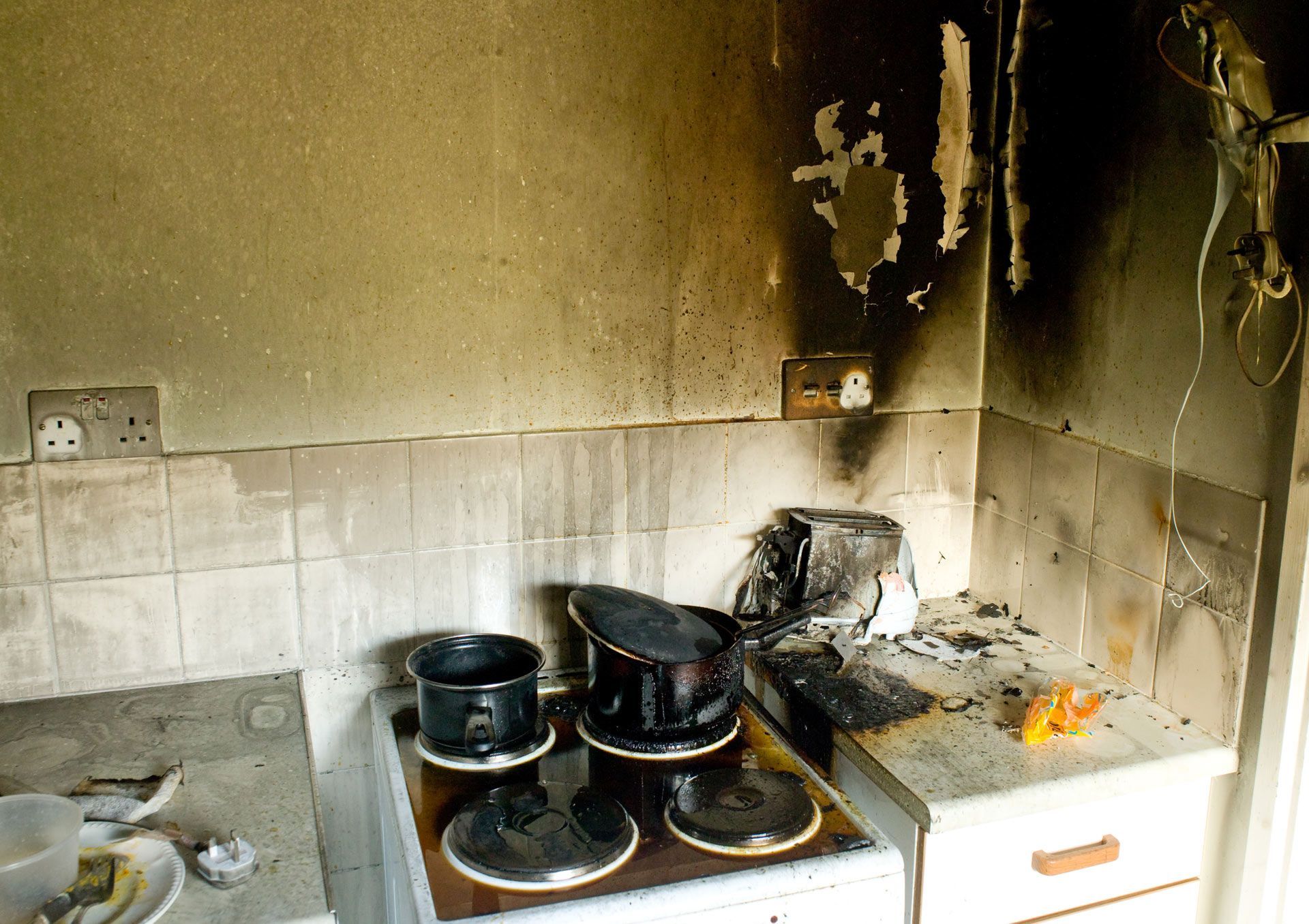 Kitchen interior severely damaged by fire; burnt appliances and walls.