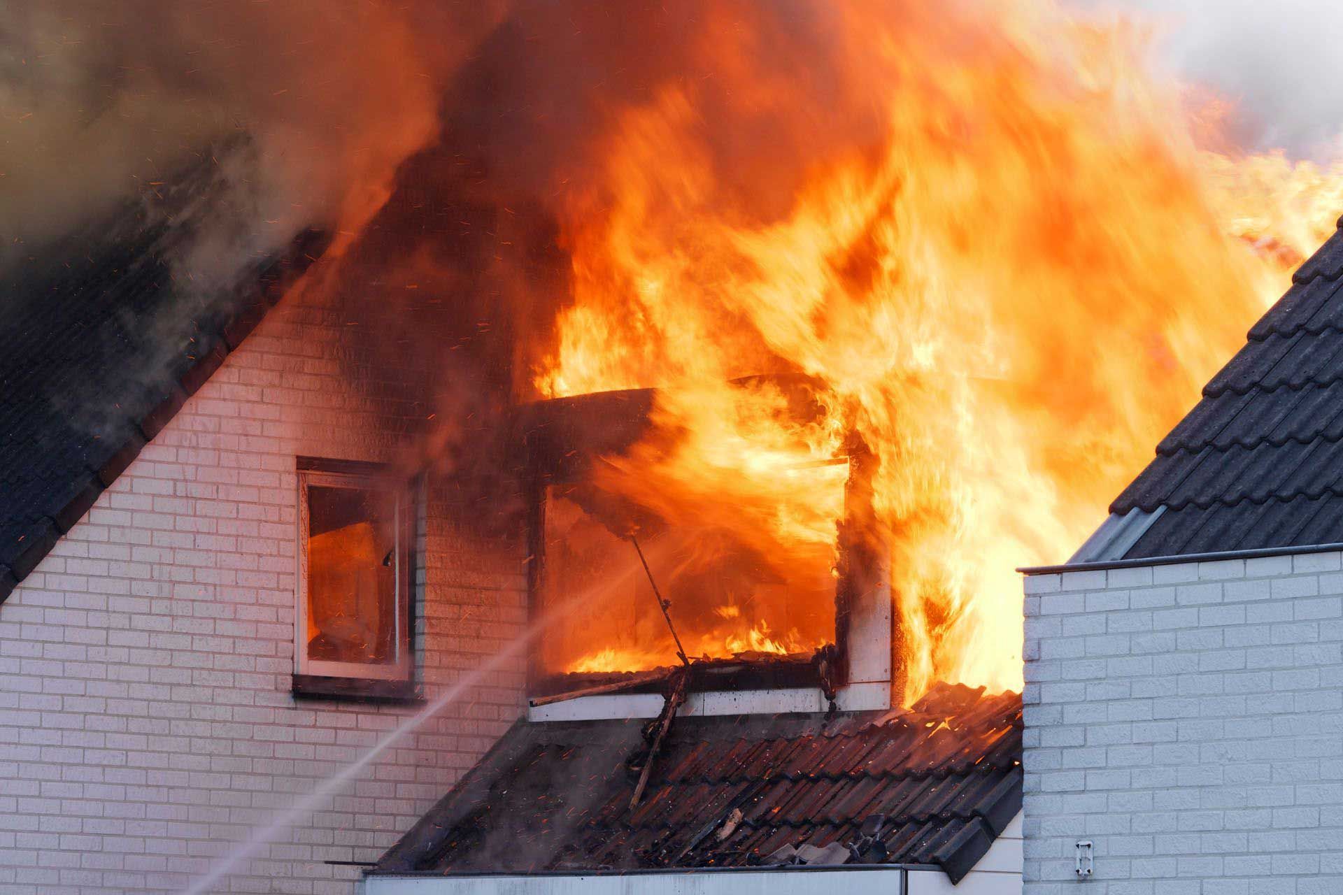 House engulfed in flames; fire visible from window and roof.