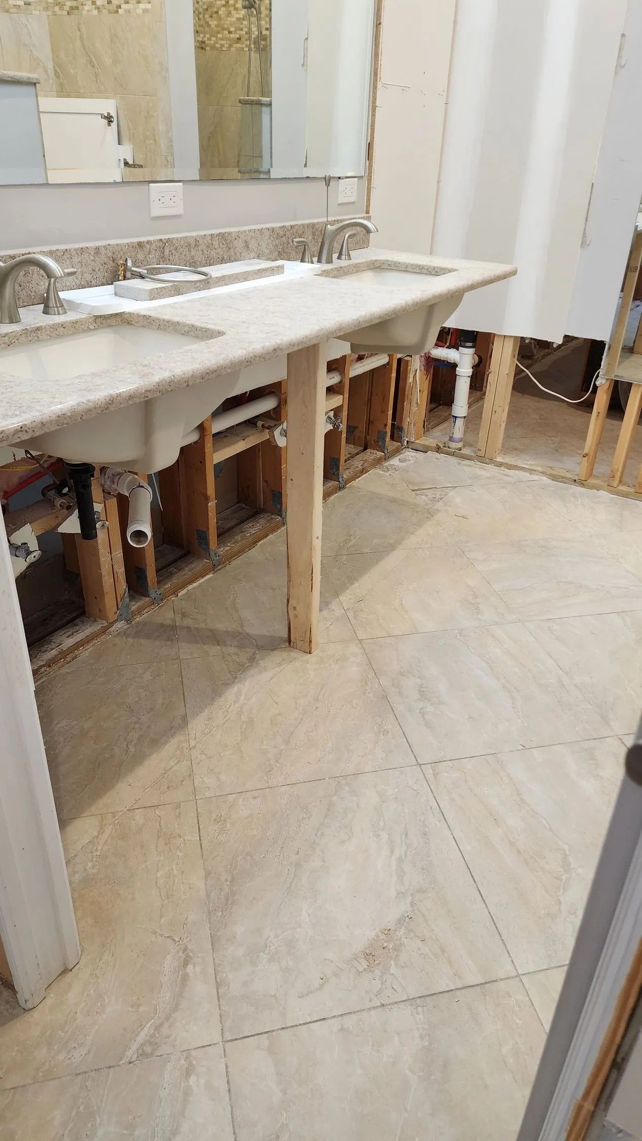 Bathroom under renovation with vanity, exposed plumbing and floor tiles.
