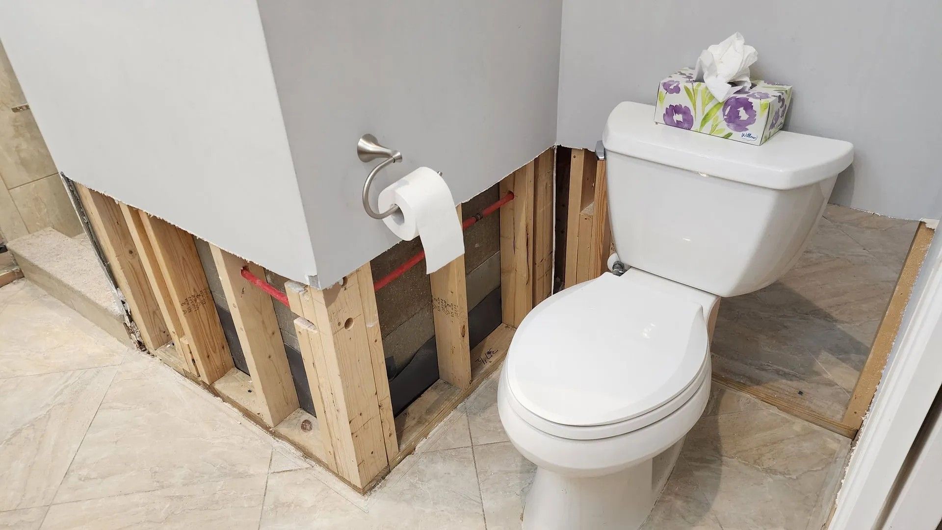 Bathroom wall with exposed studs next to a toilet, likely due to water damage.