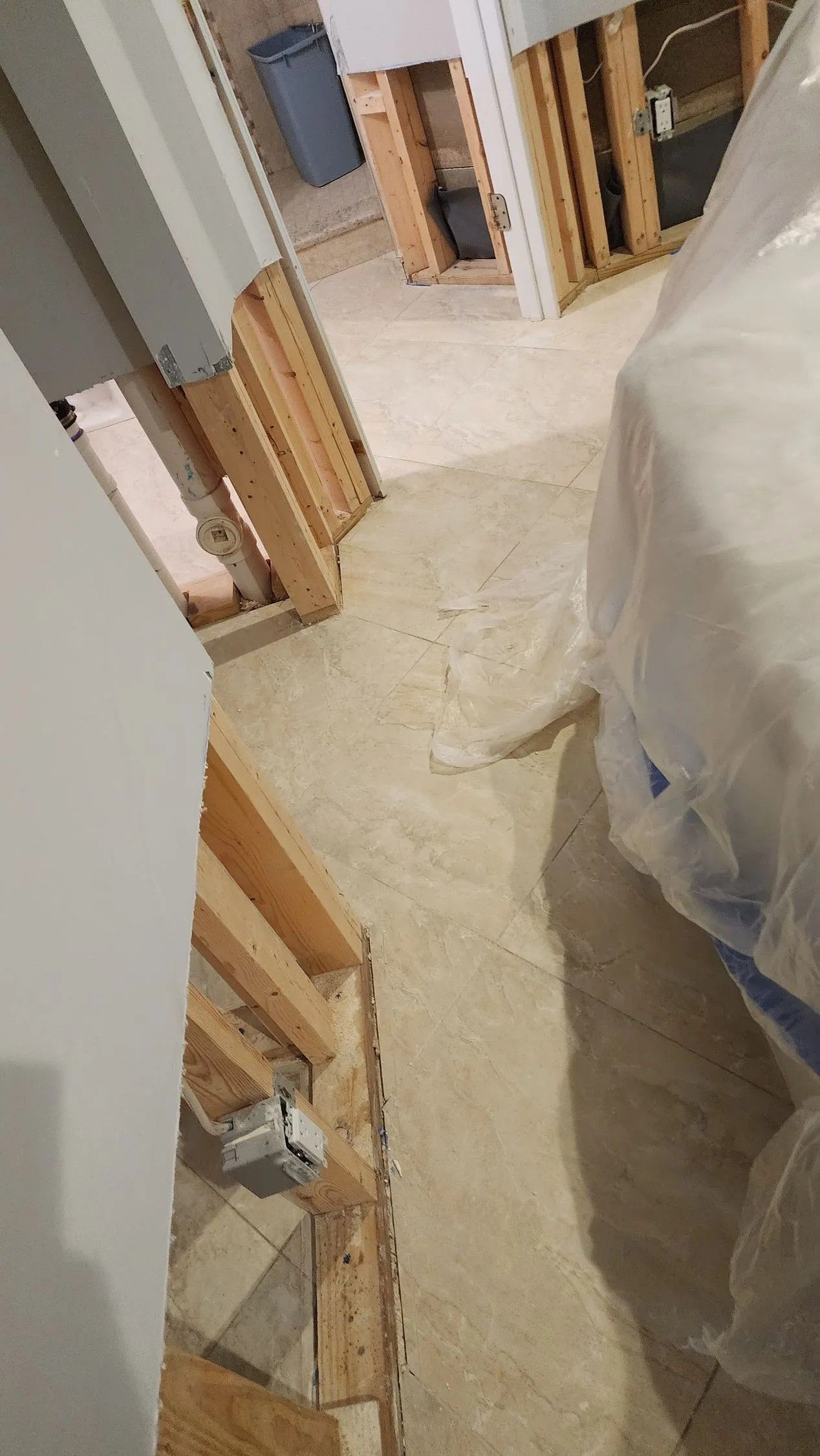 Basement under construction, exposed wood framing, concrete floor, white plastic-covered furniture, electrical outlet visible.