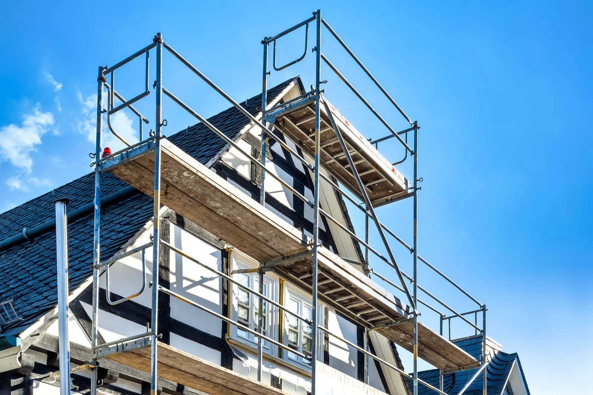 Scaffolding set up against a half-timbered house for exterior work, against a blue sky.