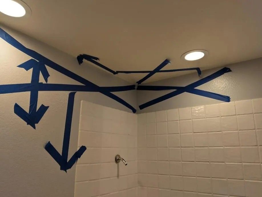 Blue tape with arrows on a white wall and ceiling, likely for a painting project, inside a shower stall.