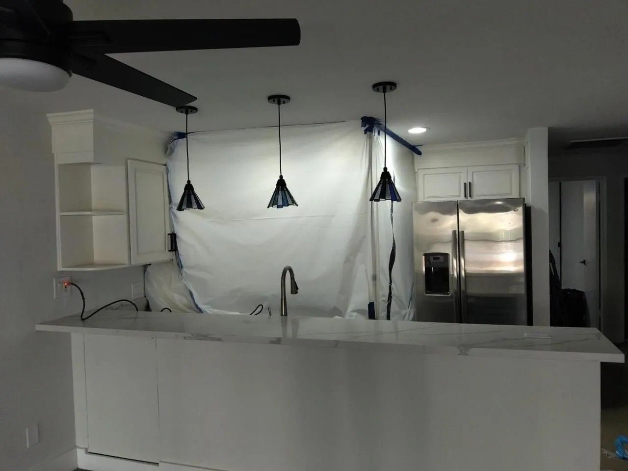 Kitchen with white cabinets, island, and pendant lights. Stainless steel refrigerator visible.