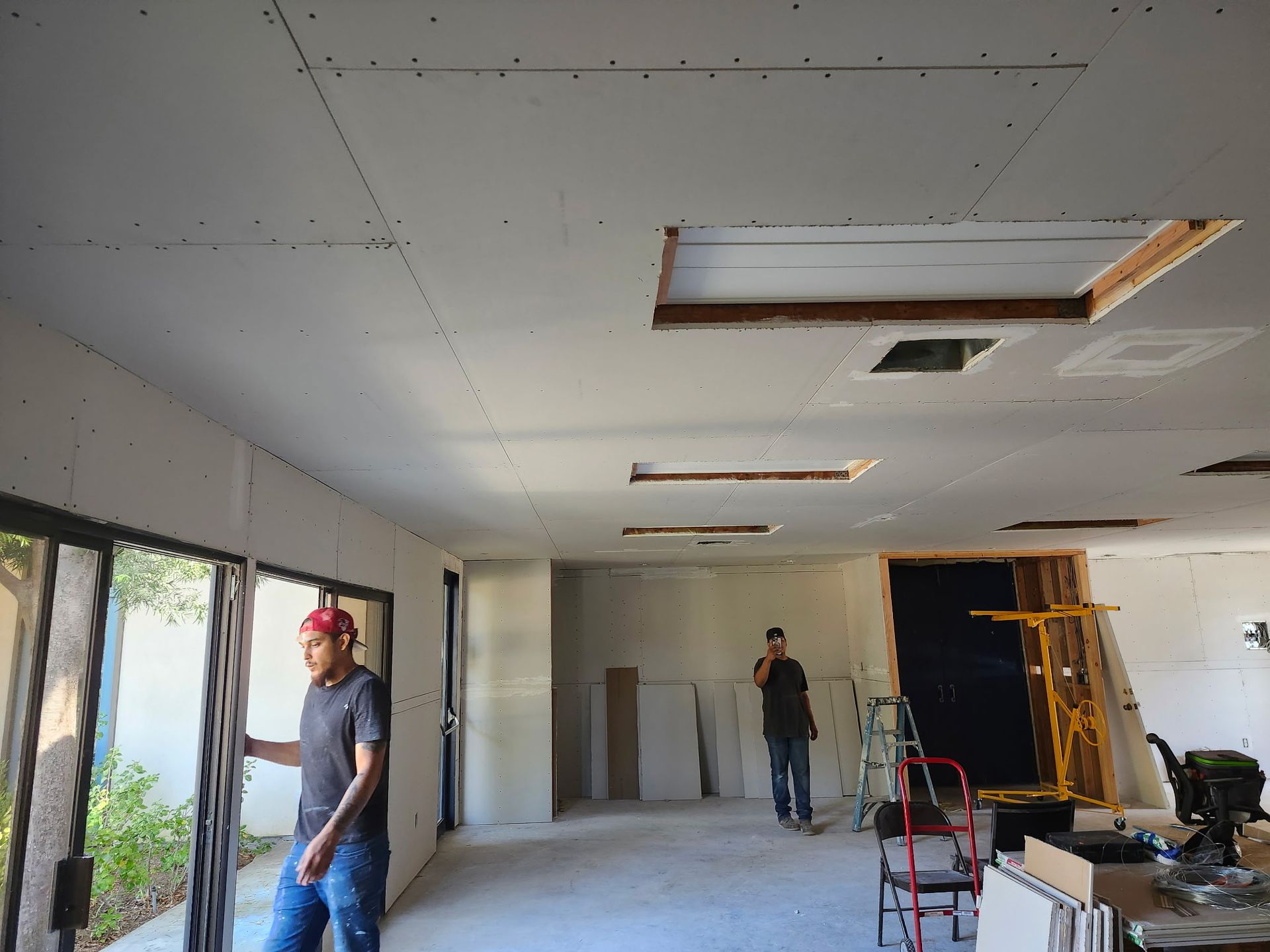 Room under construction. Drywall ceiling with openings, men working.