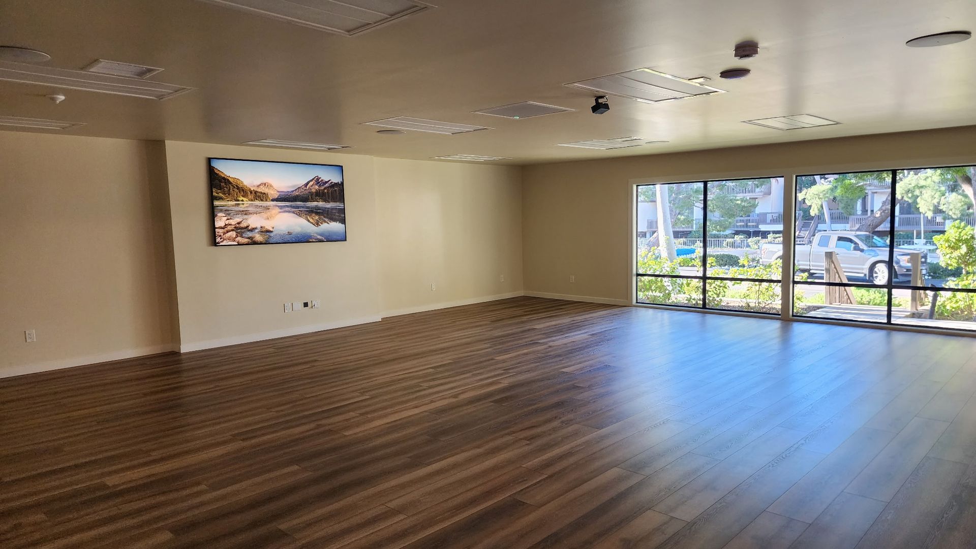 Empty room with wood floor, large windows, and a landscape painting on the wall.