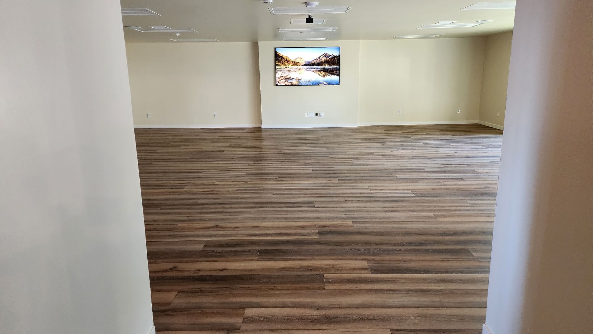 Empty room with light wood floors, beige walls, and a landscape painting.
