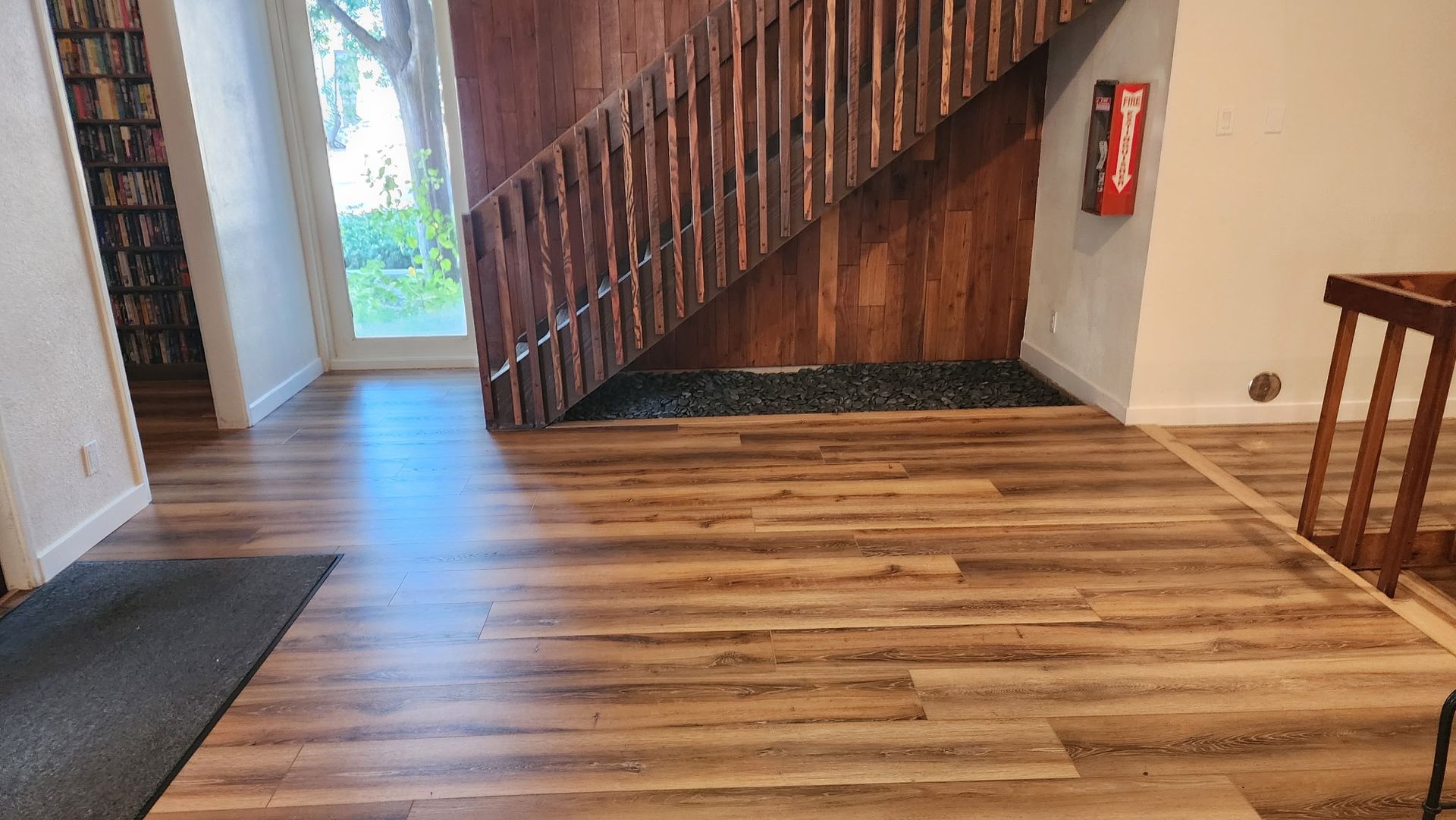 Hallway with wood floors, stairs, and a door to the outdoors. A fire extinguisher hangs on the wall.