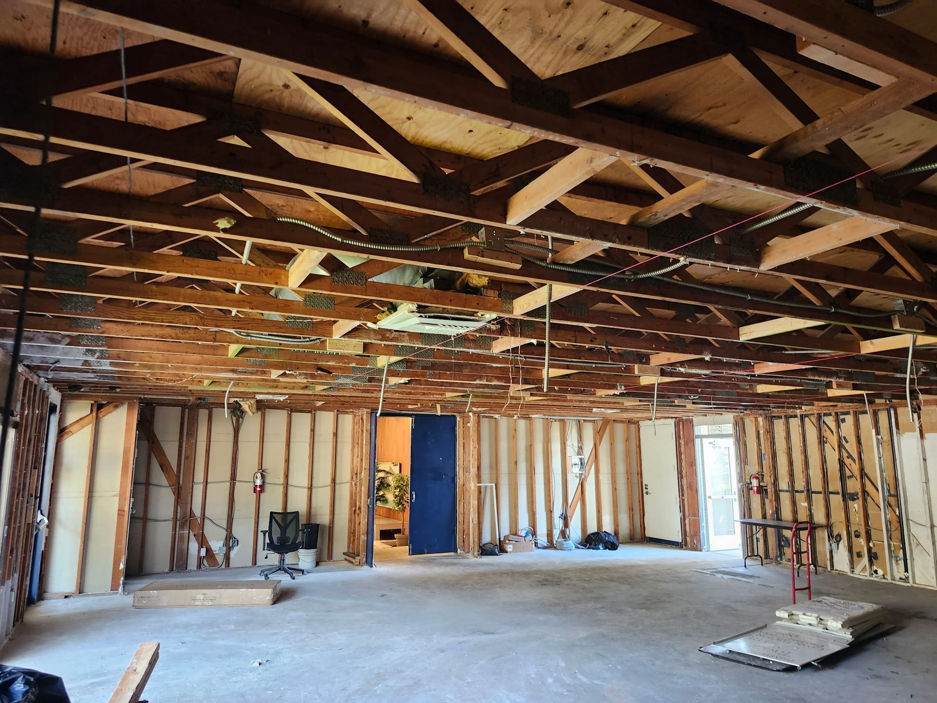 Interior of a room under renovation. Exposed wooden beams and studs, open ceiling, bare walls, and concrete floor.