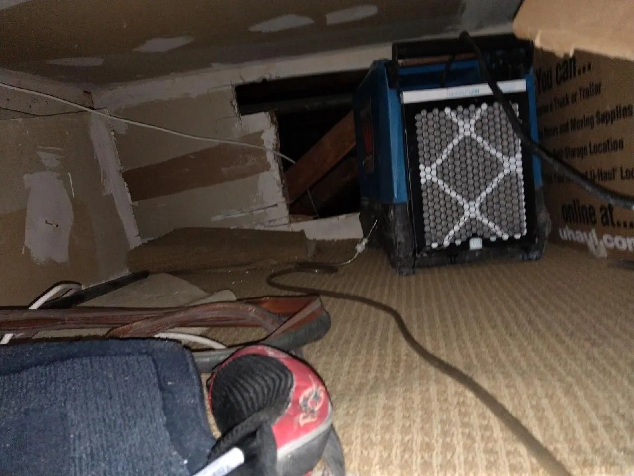Blue dehumidifier in a crawlspace with damage and exposed wires.