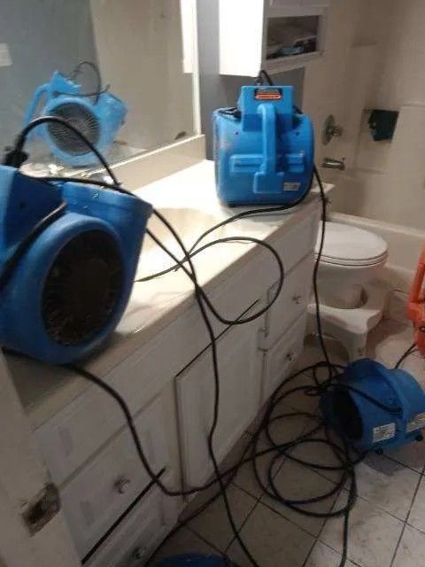 Three blue fans in a bathroom, likely drying a flooded area. Electrical cords are visible.