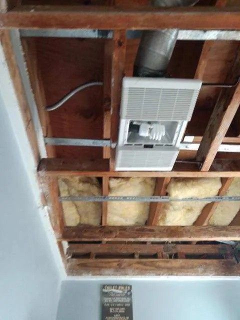 Open ceiling with vent fan, ductwork, insulation, and wood beams.