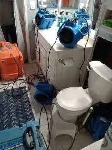 Dehumidifiers drying out a flooded bathroom. Includes toilet, cabinets, and various machines.
