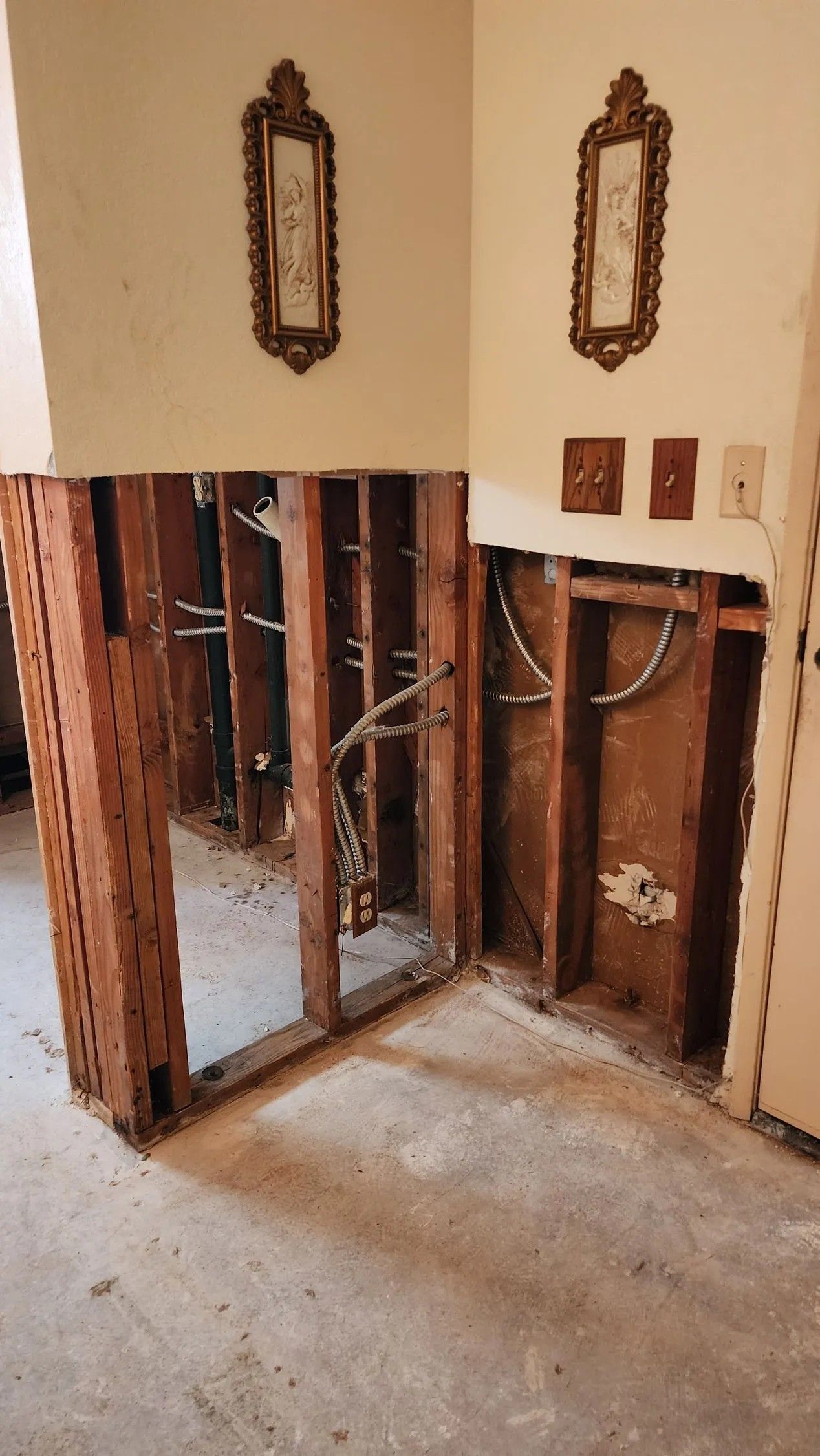 Interior room with exposed wall studs, electrical wiring, and damage, below two framed pictures.