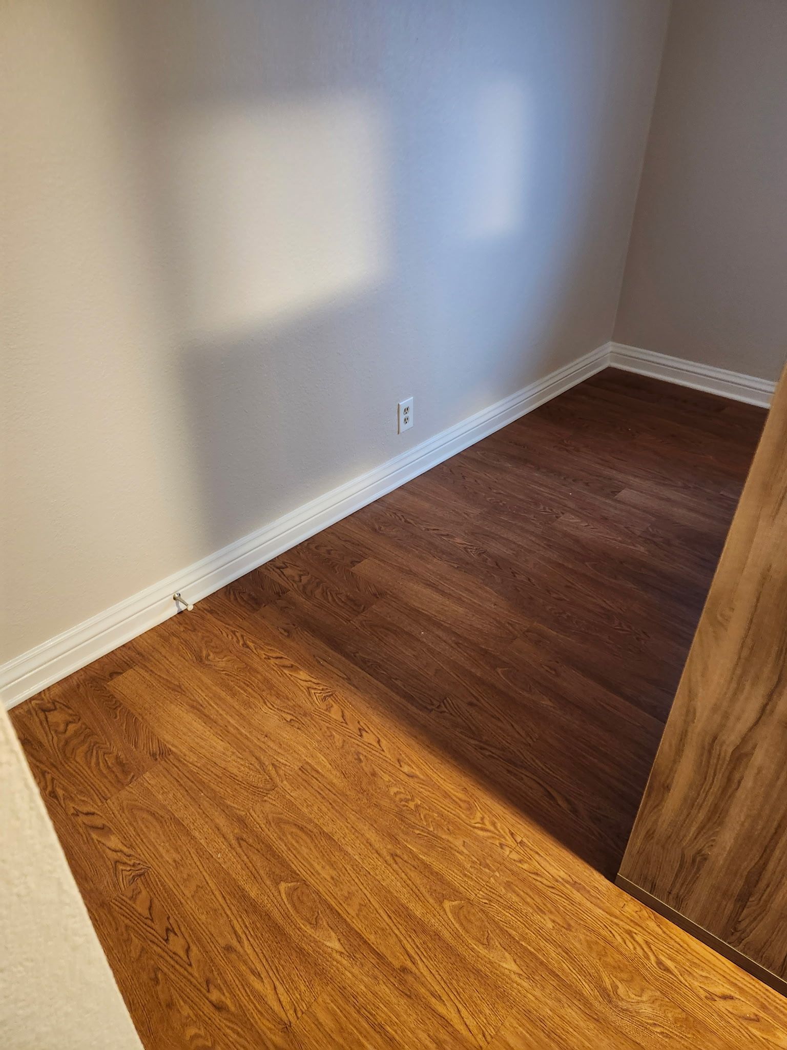 Hardwood flooring installed in a corner room, next to a white baseboard and tan walls.