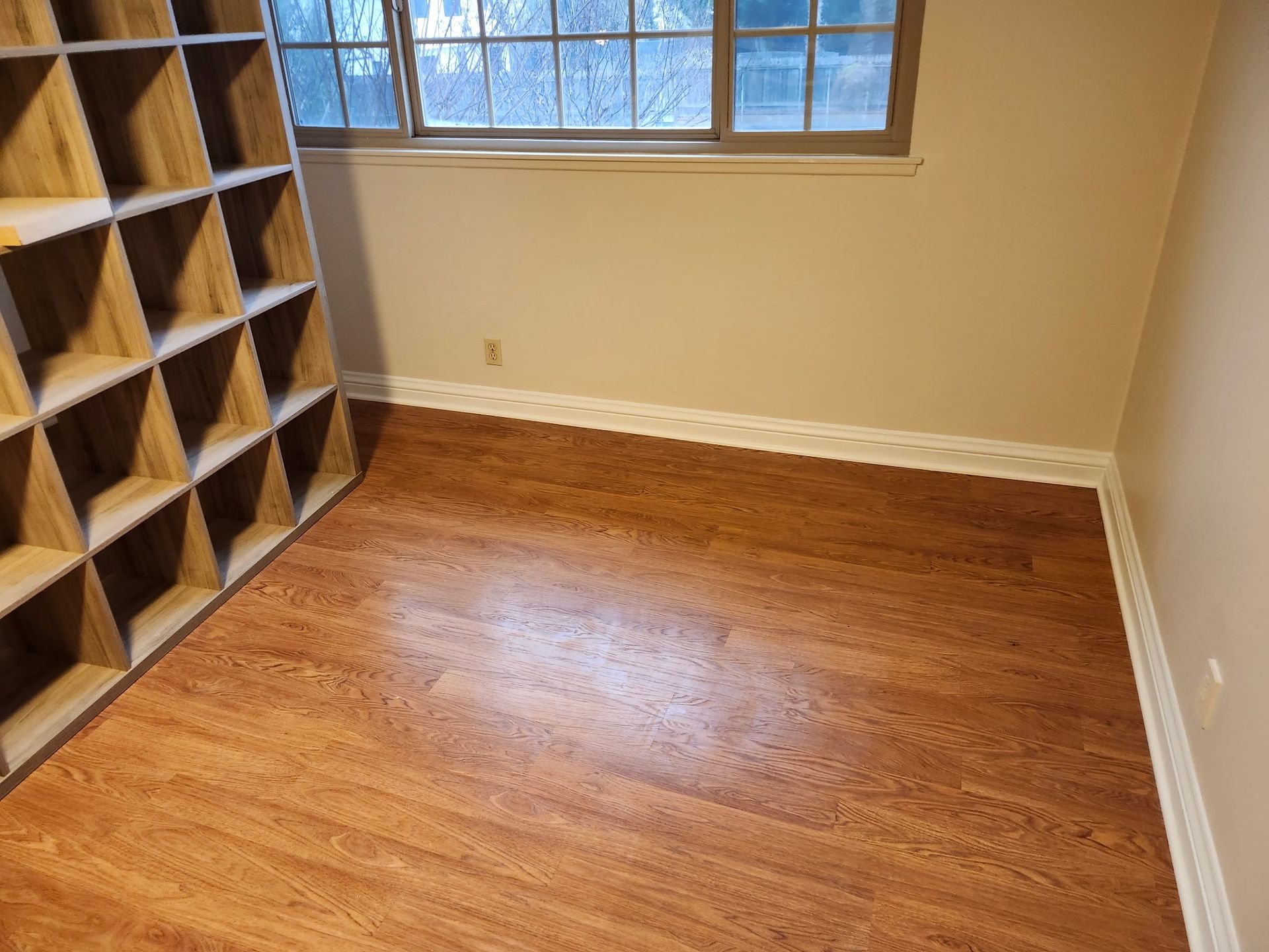 Room with wood-look flooring, beige walls, a window, and a cubby-style shelving unit on the left.