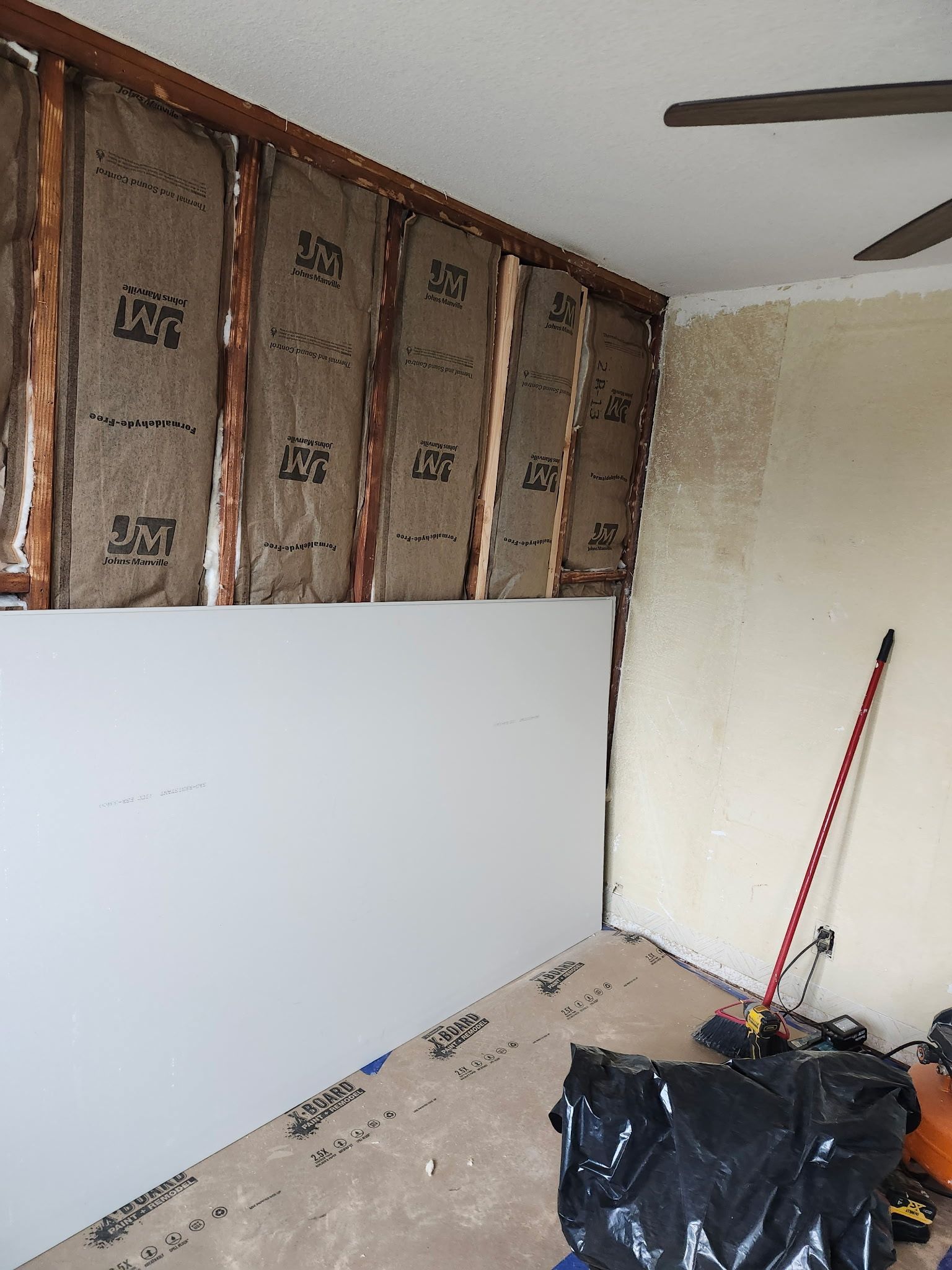 Room under renovation; exposed wall studs with insulation, drywall, and debris.