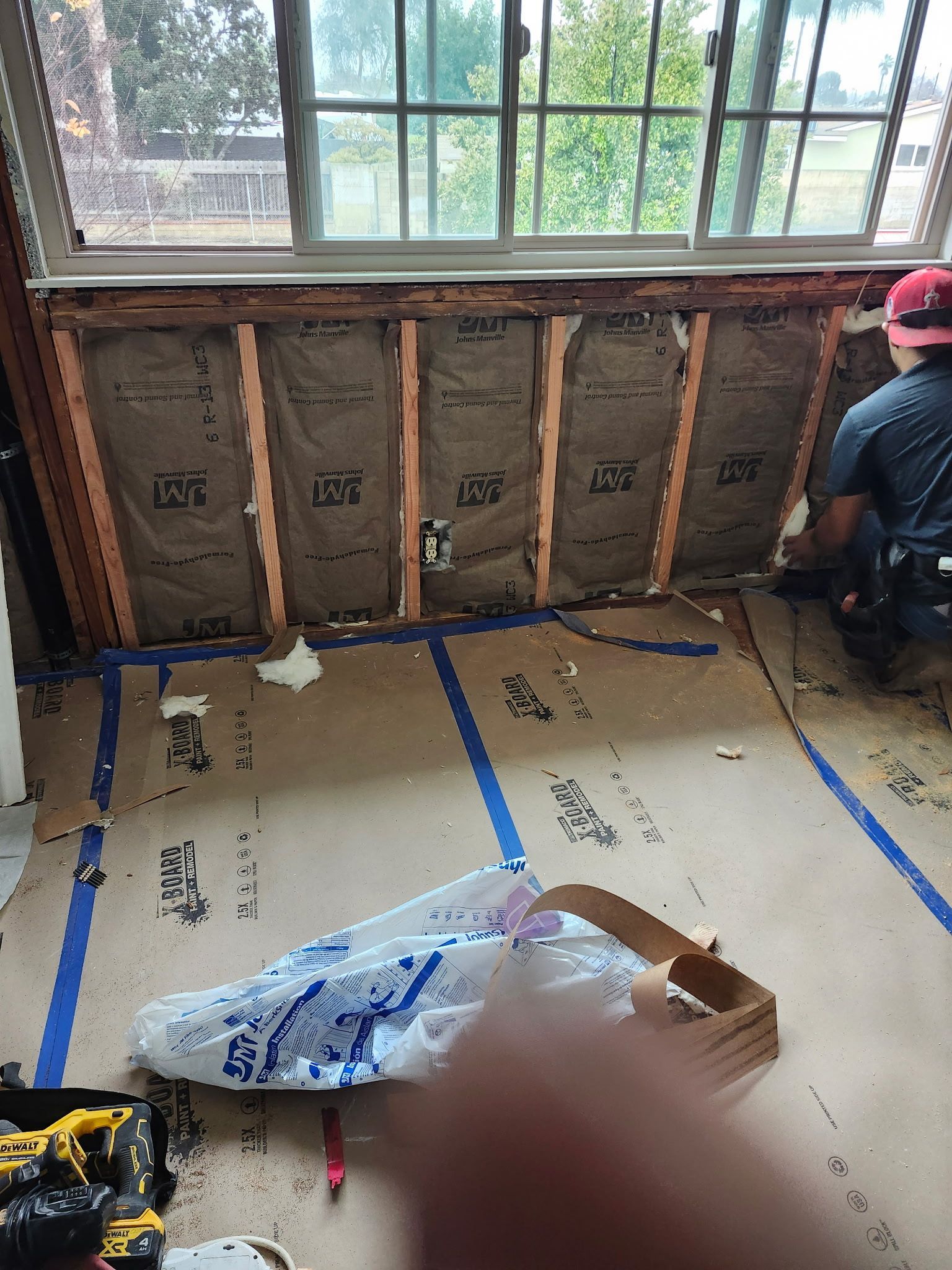 Interior wall under construction with insulation between wood studs, person working.