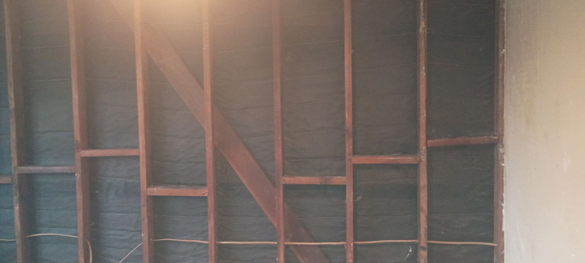 Exposed wall studs with diagonal support beam, dark backing material. Light falls on the upper left side.