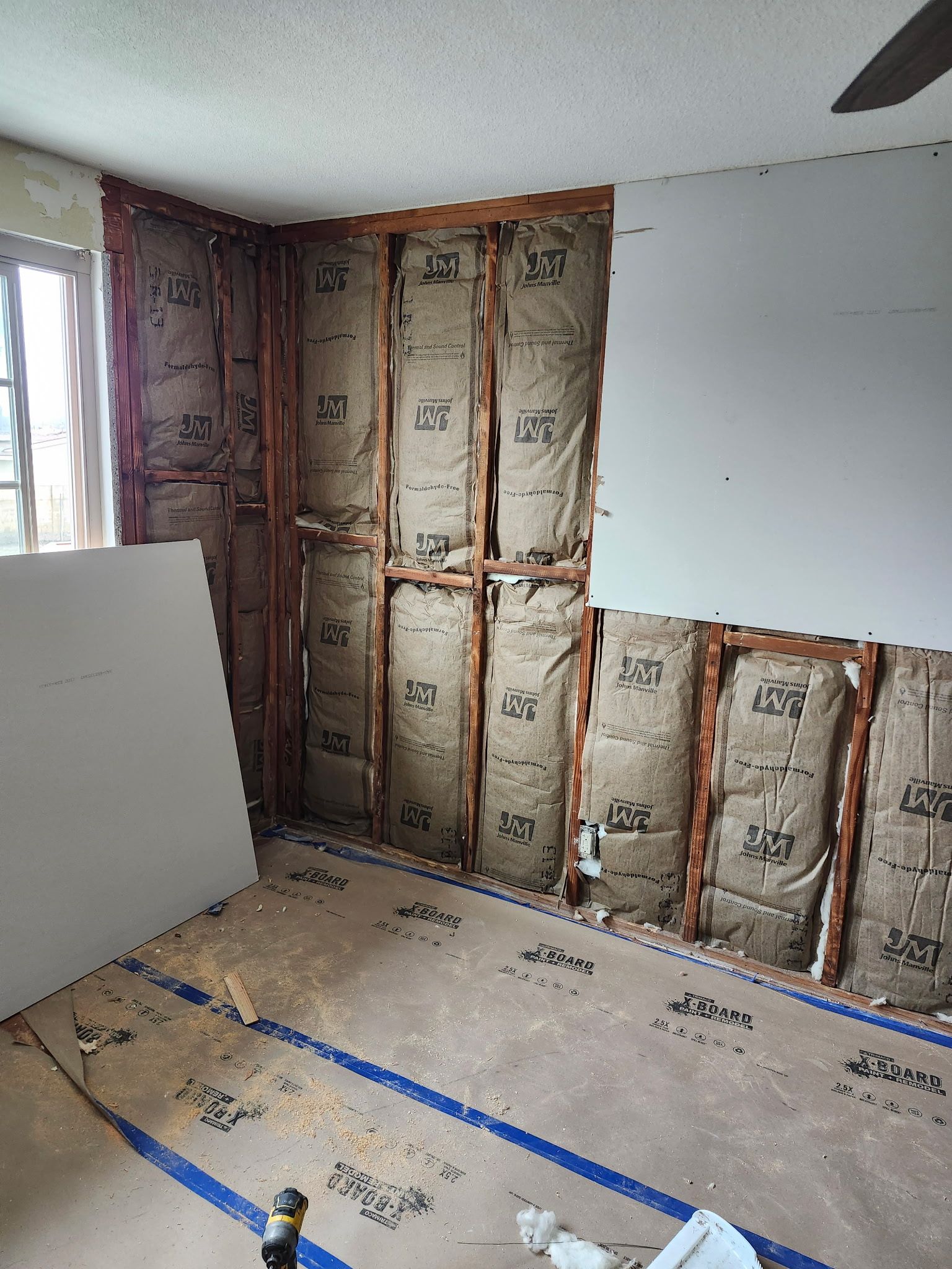 Interior room under construction, with exposed insulation in the walls, drywall, and a dusty floor.