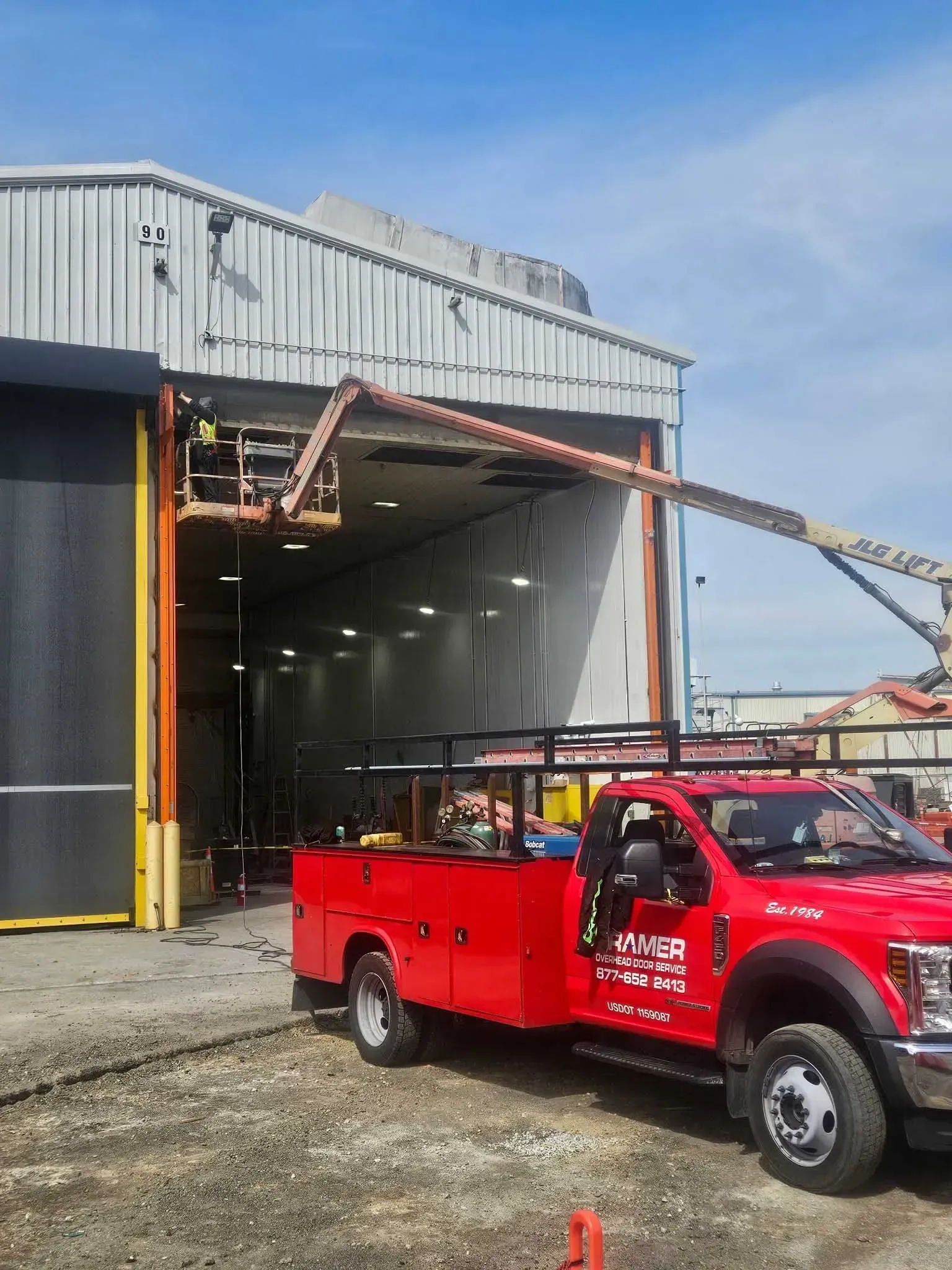 Red service truck with lift in front of a building. Workers use the lift to work on the building's roof.