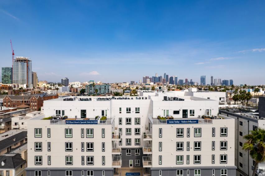 Fedora - white apartment buildings with a city skyline under a bright blue sky.