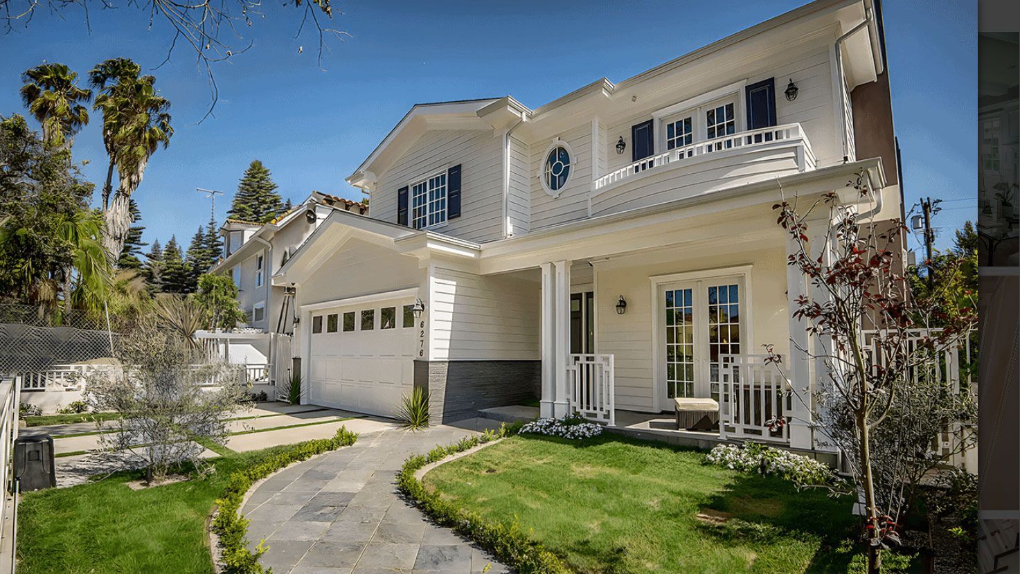 White two-story house with a gray stone pathway leading to the front door. Palm trees and green grass surround the home.