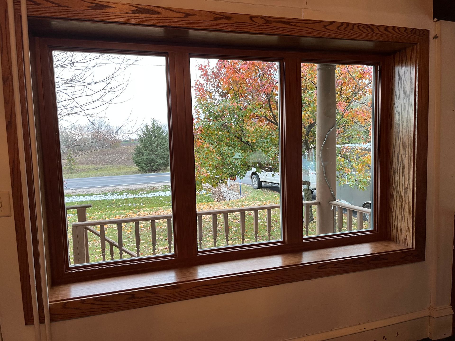 Wood-framed window overlooking a yard with autumn trees and a river beyond