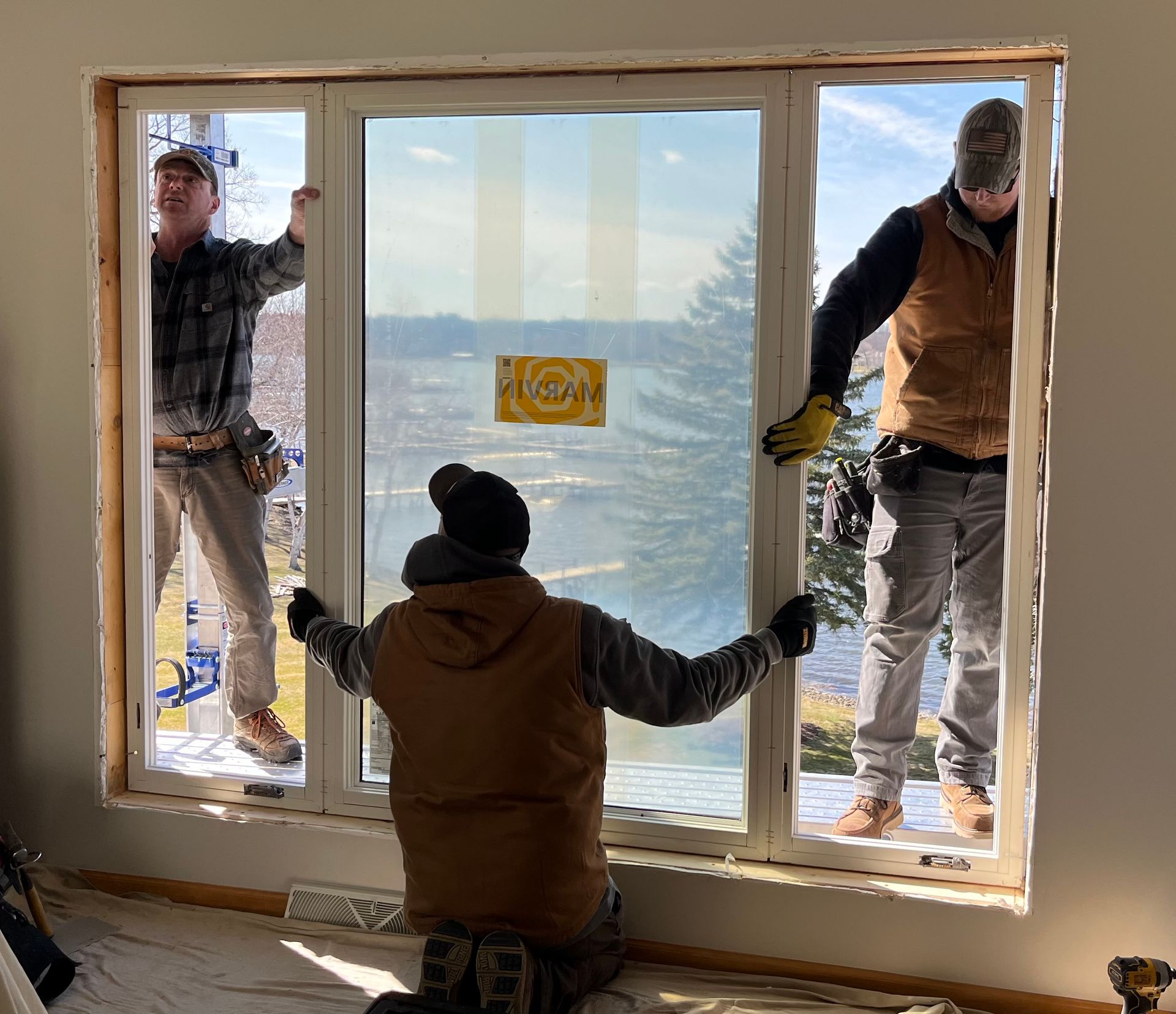 Three workers install a large window frame inside a room with a snowy mountain view.