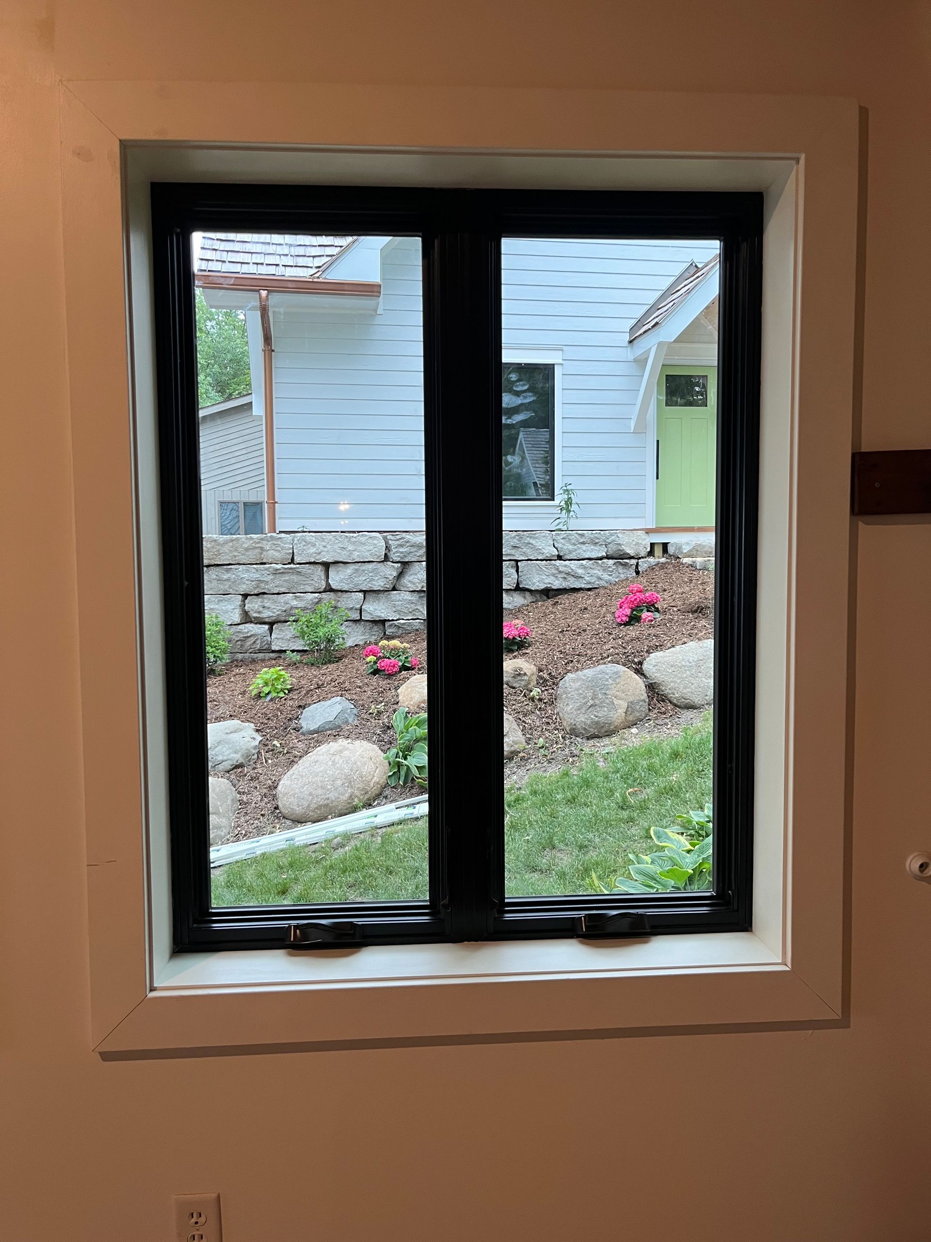 Small black-framed window looking onto a garden and the side of a house